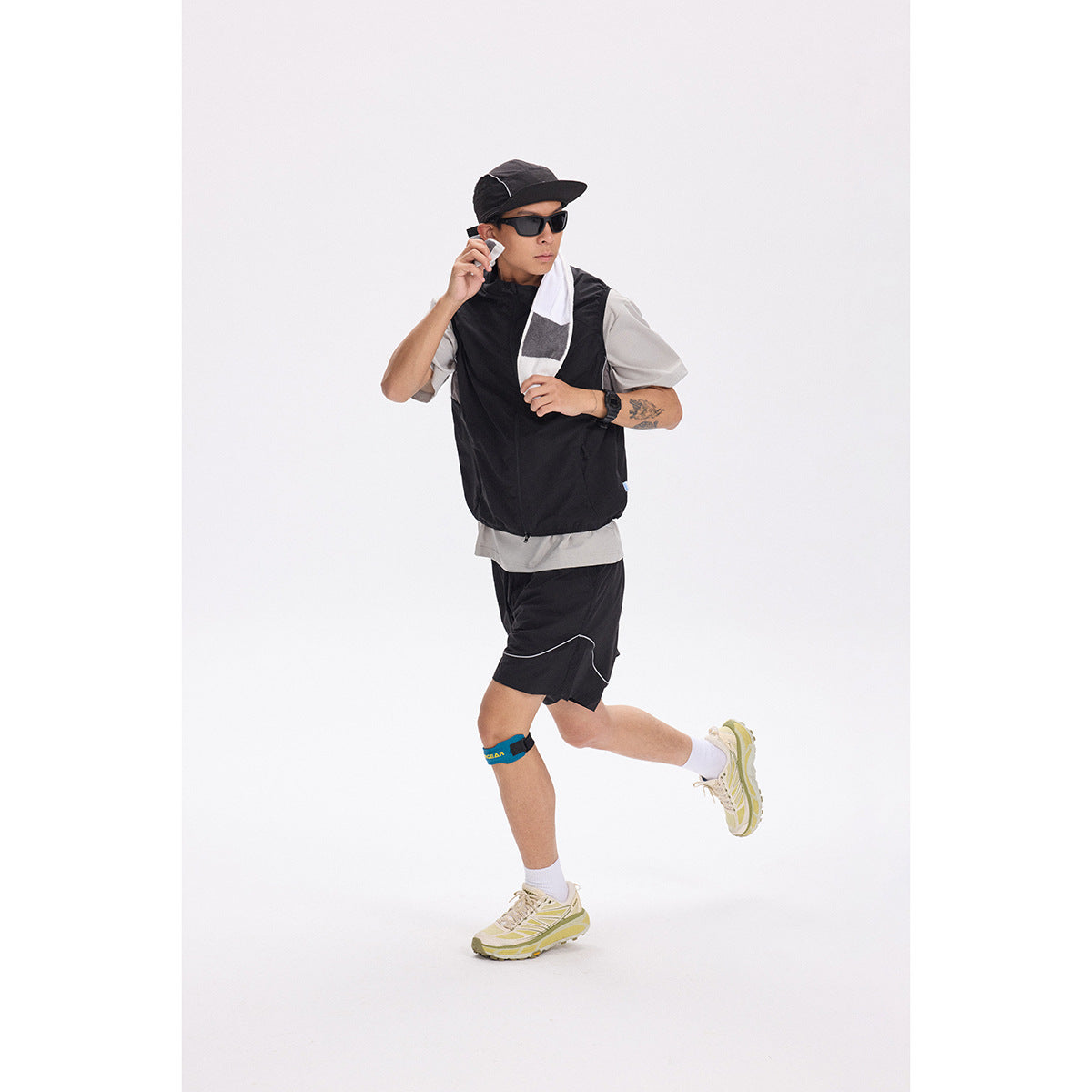 Runner wearing a black zip vest over a gray shirt with black shorts and a black cap.