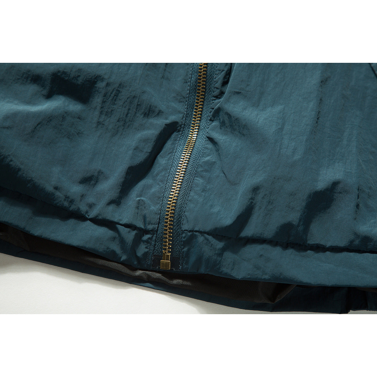 Close-up of the dark teal jacket's brass-tone zipper near the bottom hem.