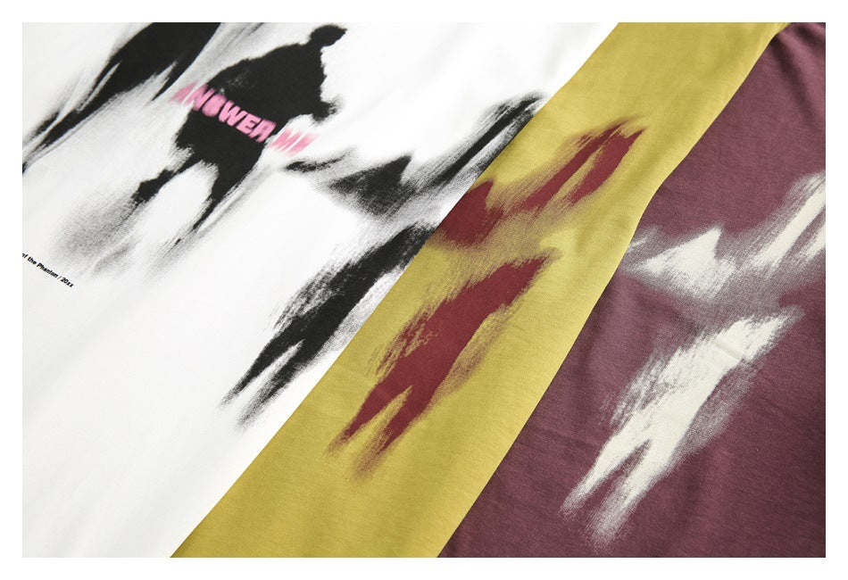 Close-up of white, mustard-yellow, and burgundy shirts with abstract brushstroke prints; the white print includes pink ANSWER