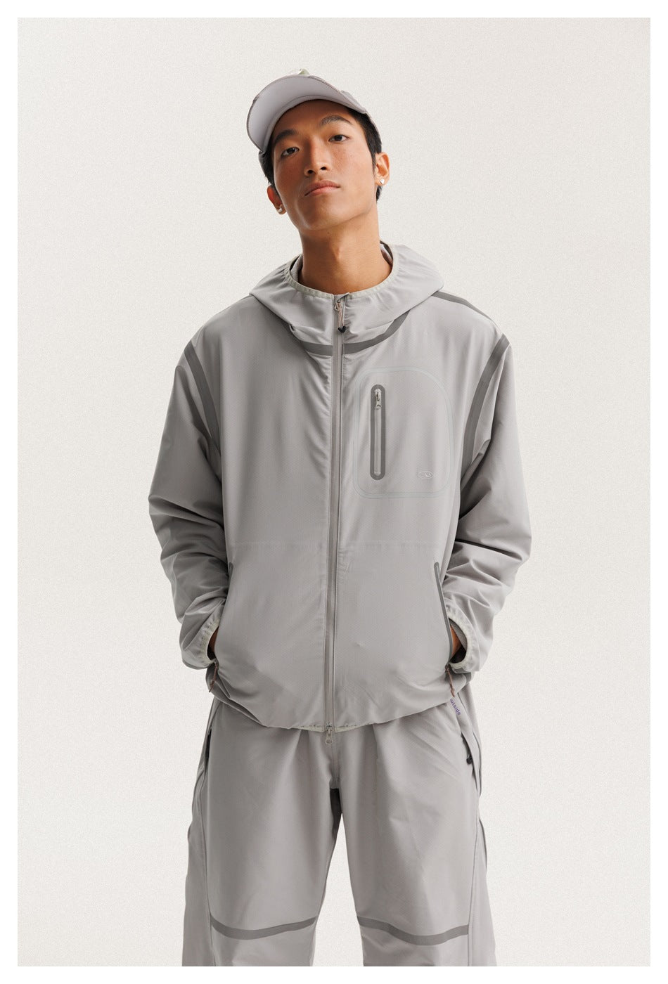 Front view of a model wearing a light gray hooded zip jacket with darker trim and matching pants.