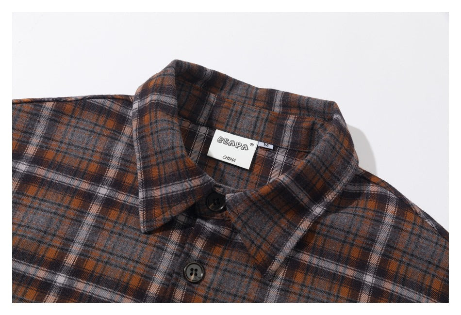Close-up of a gray, rust, and black plaid shirt collar with dark buttons and a sewn neck label.