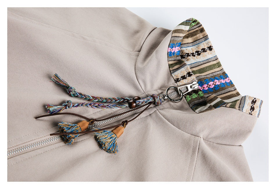 Beige jacket close-up showing its patterned collar, silver zipper, and multicolor braided tassel pulls.