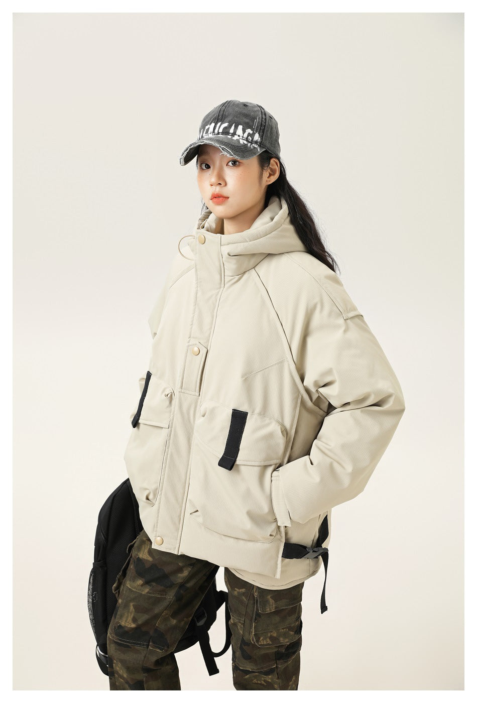 Angled view of a model wearing a light cream hooded jacket with large flap pockets and black accents.