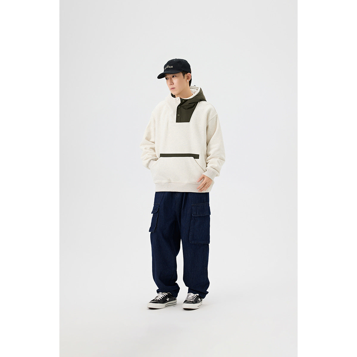 Full-length view of a model wearing an ivory and olive pullover hoodie with dark cargo jeans.
