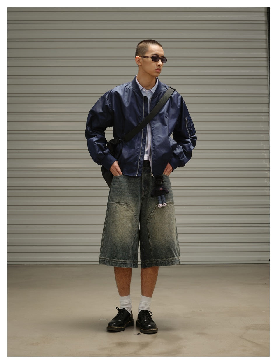 Front view of a model wearing a navy bomber jacket, black crossbody strap, and oversized faded denim shorts.