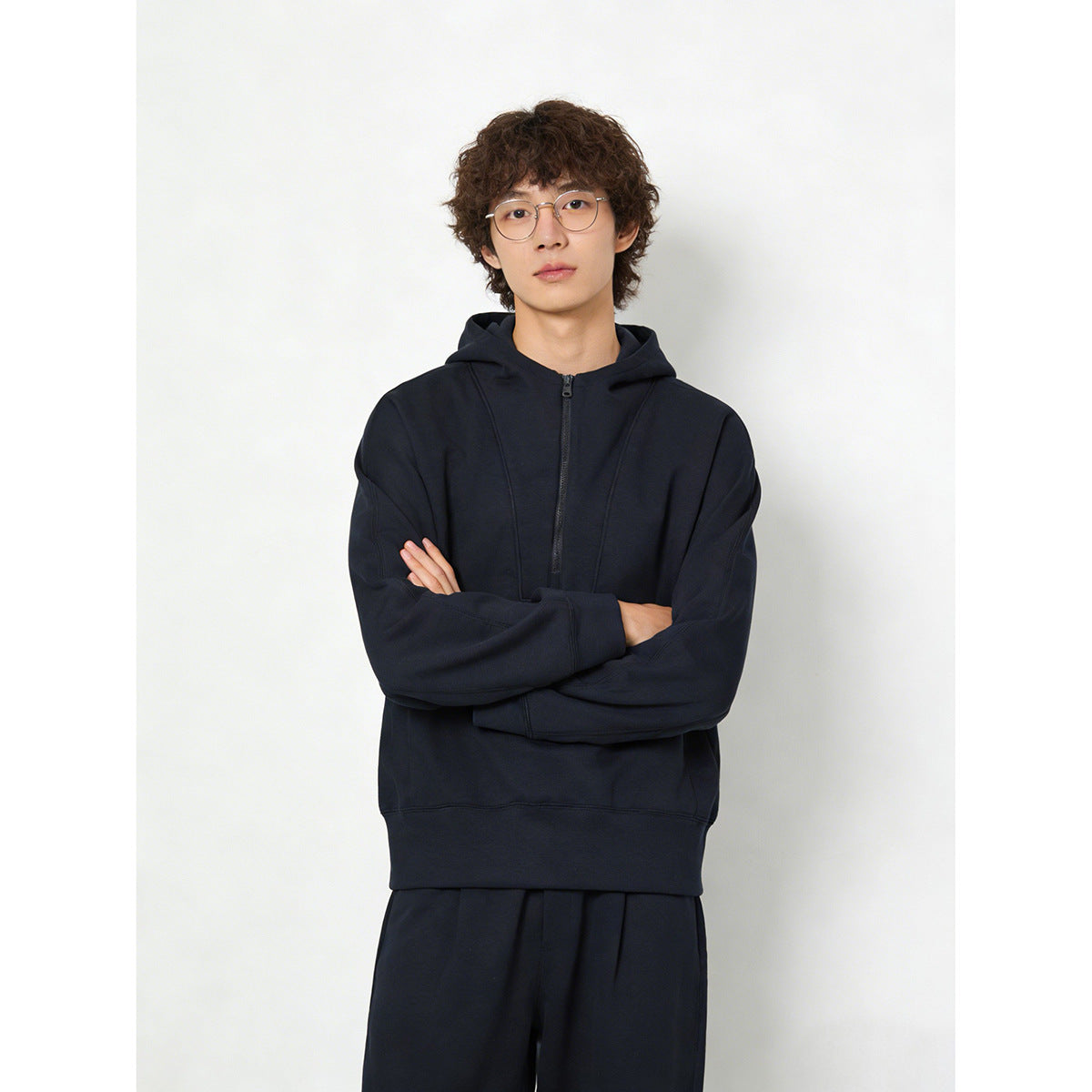 Model wearing a dark navy hooded pullover with a short front zipper and matching pants.