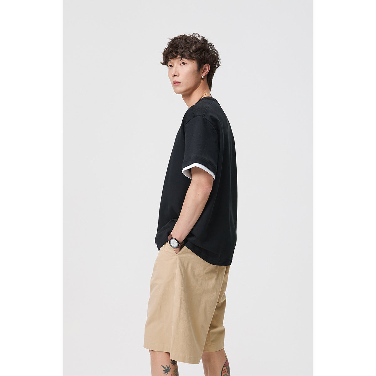 Side view of a model wearing a black oversized T-shirt with white sleeve layers and beige shorts.