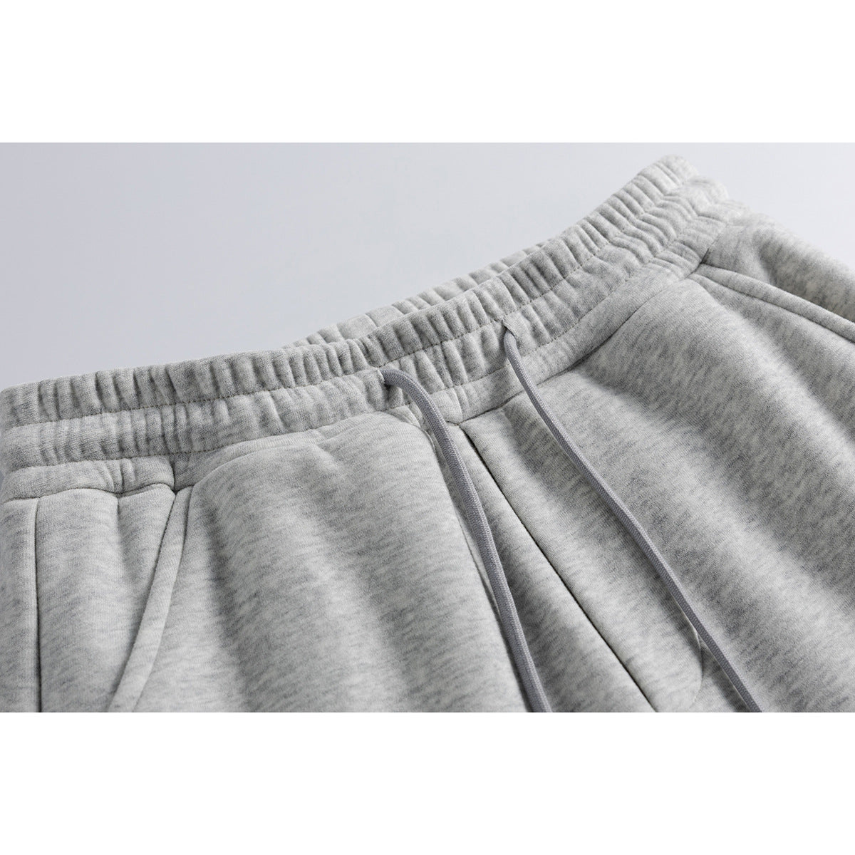 Close-up of light gray sweatpants with an elastic waistband, matching drawstrings, and a slanted pocket.