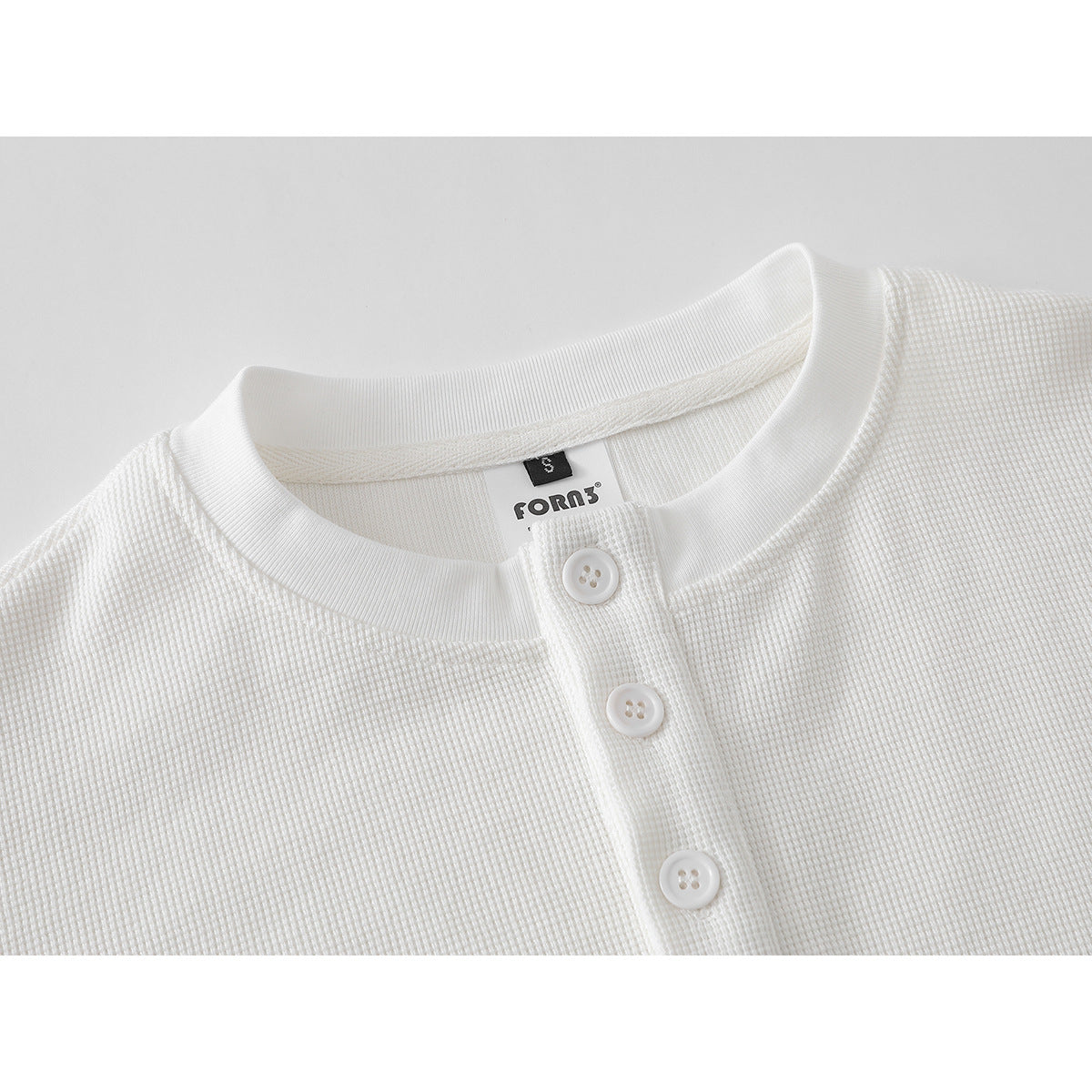 Close-up of a white textured shirt neckline with a short three-button placket and ribbed collar.