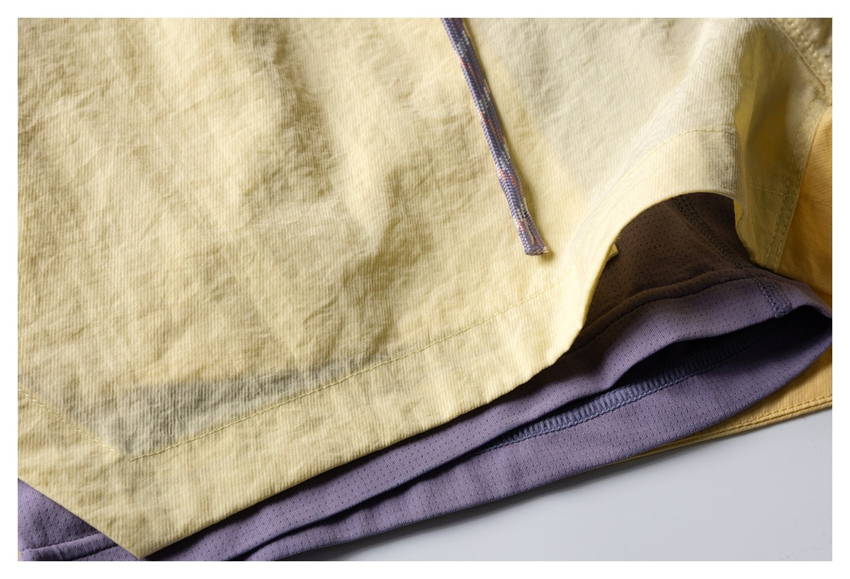 Close-up of pale yellow shorts showing the hem, purple mesh lining, and a drawcord.