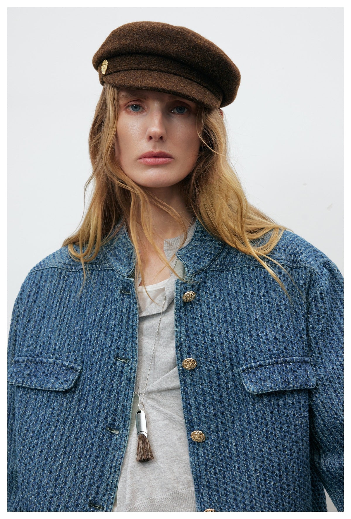 Close view of a model wearing a blue textured jacket with gold buttons and flap pockets.