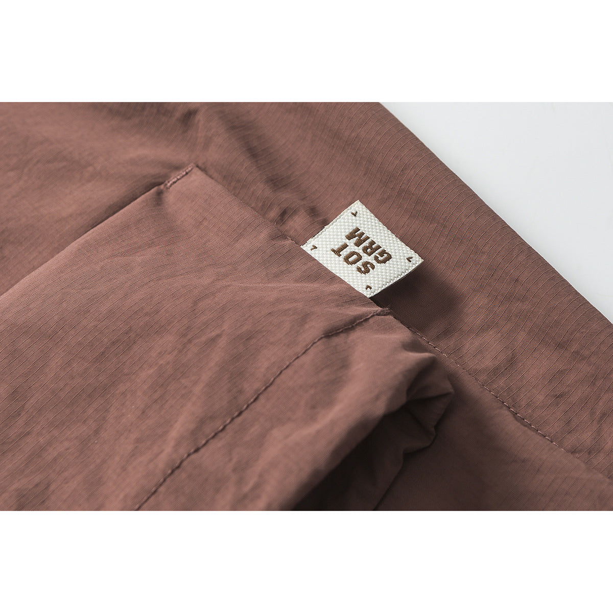 Close-up of dusty mauve shorts showing a pocket seam and a small white sewn label.