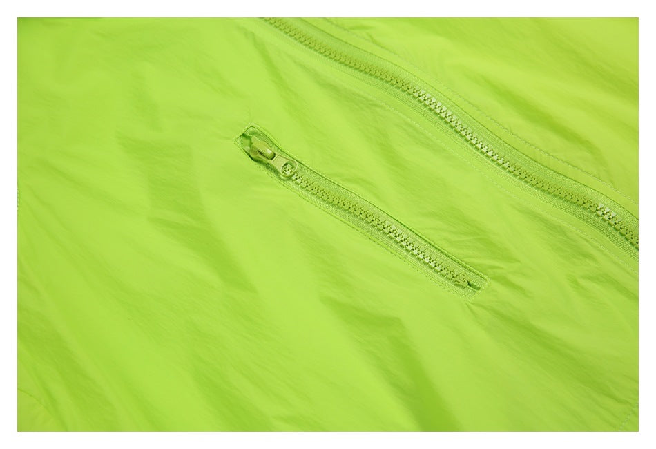 Close-up of a neon lime garment showing a long zipper and a smaller diagonal zip pocket.