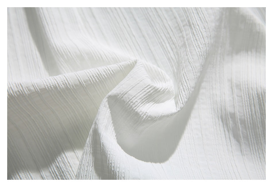 Close-up of white fabric with raised, irregular vertical stripes and a softly crumpled texture.