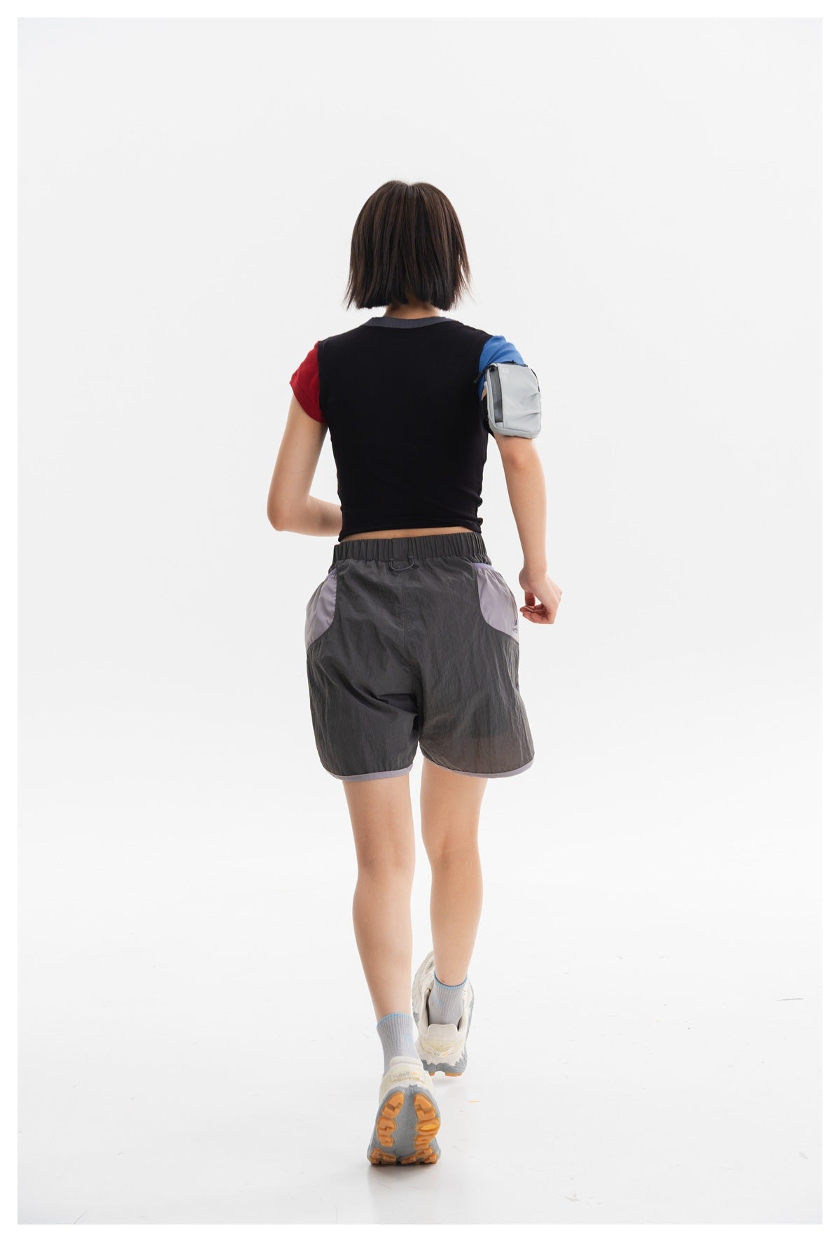 Rear view of a model wearing a black cropped top with contrasting sleeves and charcoal shorts with lavender panels.