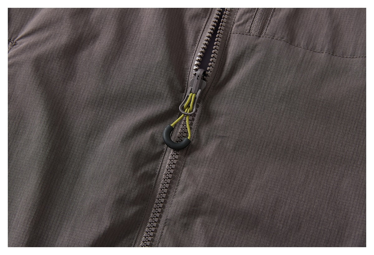Close-up of the jacket’s front zipper with a lime cord pull against dark charcoal fabric.