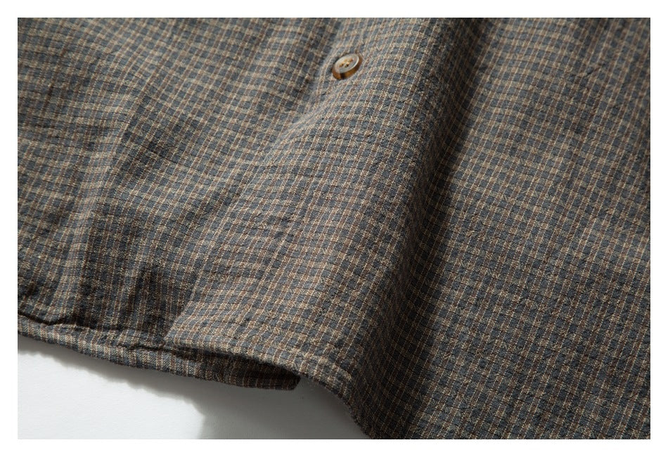 Close-up of brown, blue, and tan checked garment fabric with a small button and stitched seam.