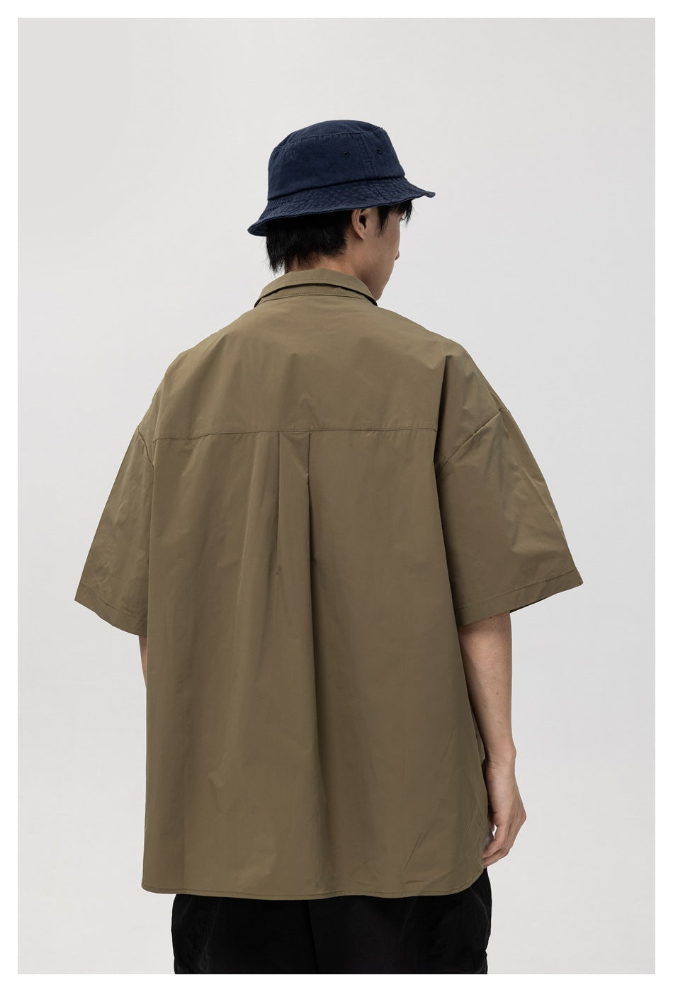 Back view of a model wearing an olive-brown short-sleeve shirt with a center pleat.