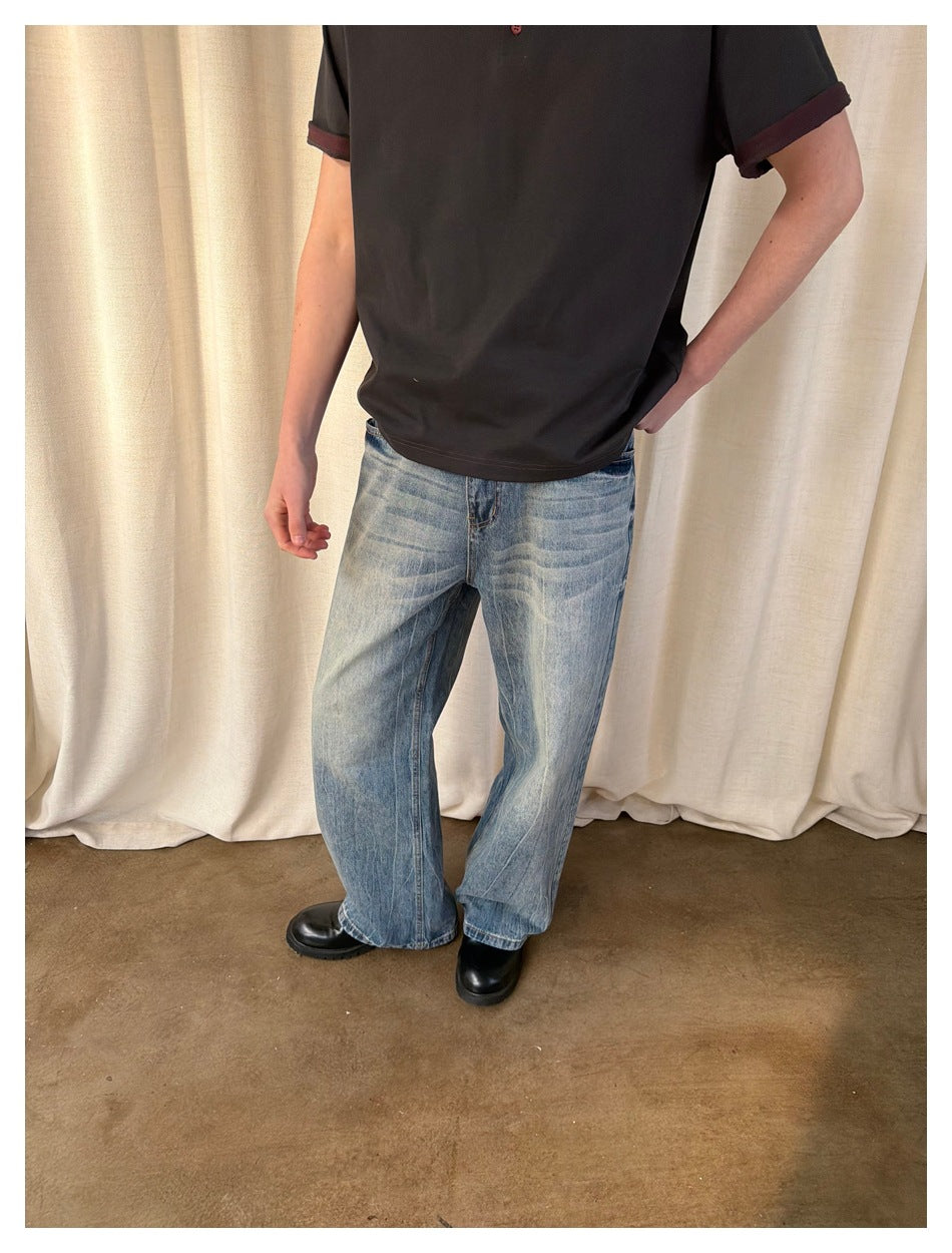 Cropped model wearing loose, faded light-blue wide-leg jeans with a dark short-sleeve shirt and black shoes.