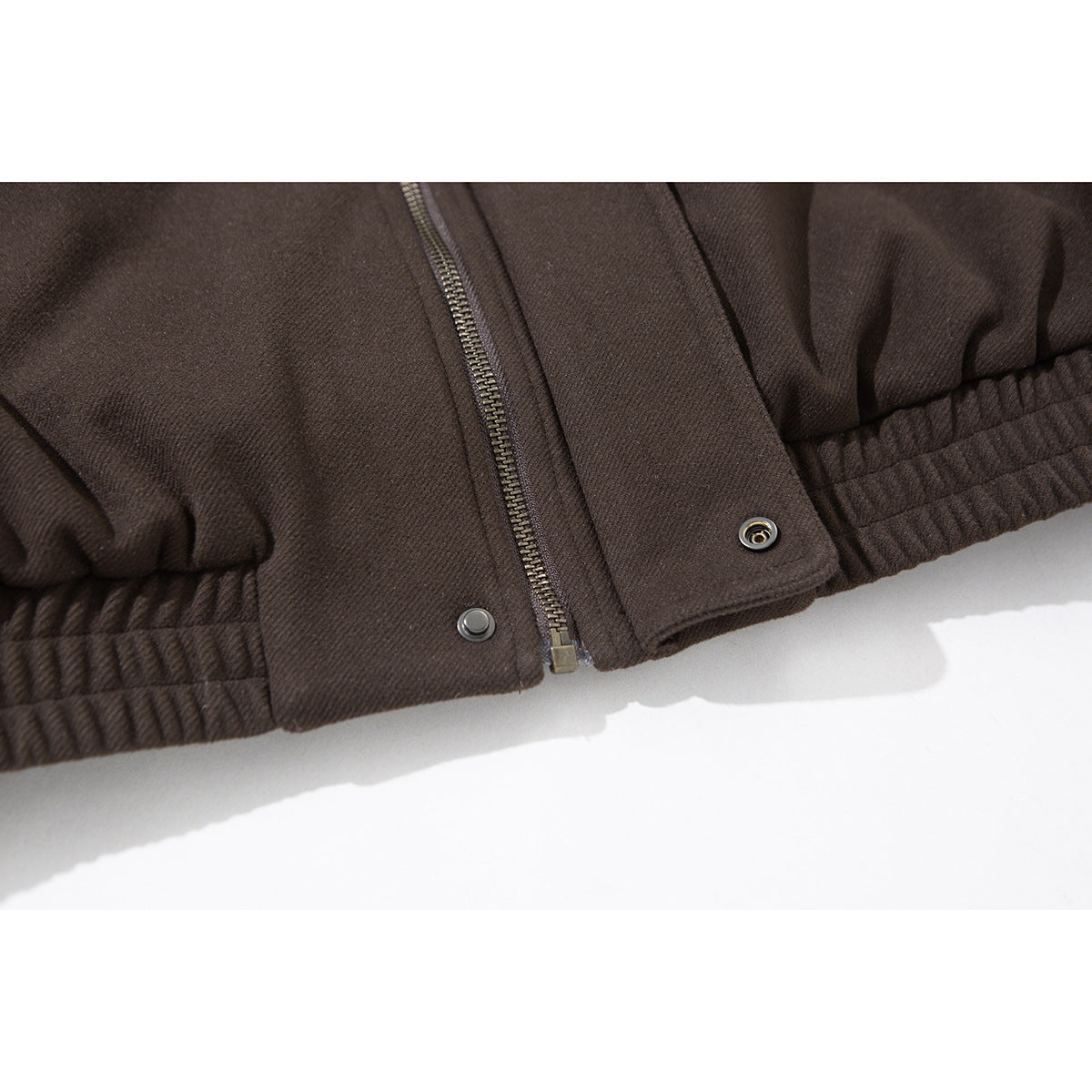 Close-up of the dark brown jacket's zip-and-snap front closure and gathered elastic hem.