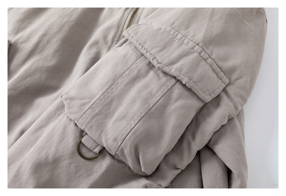 Close-up of a light taupe jacket sleeve utility pocket with a flap and metal D-ring.