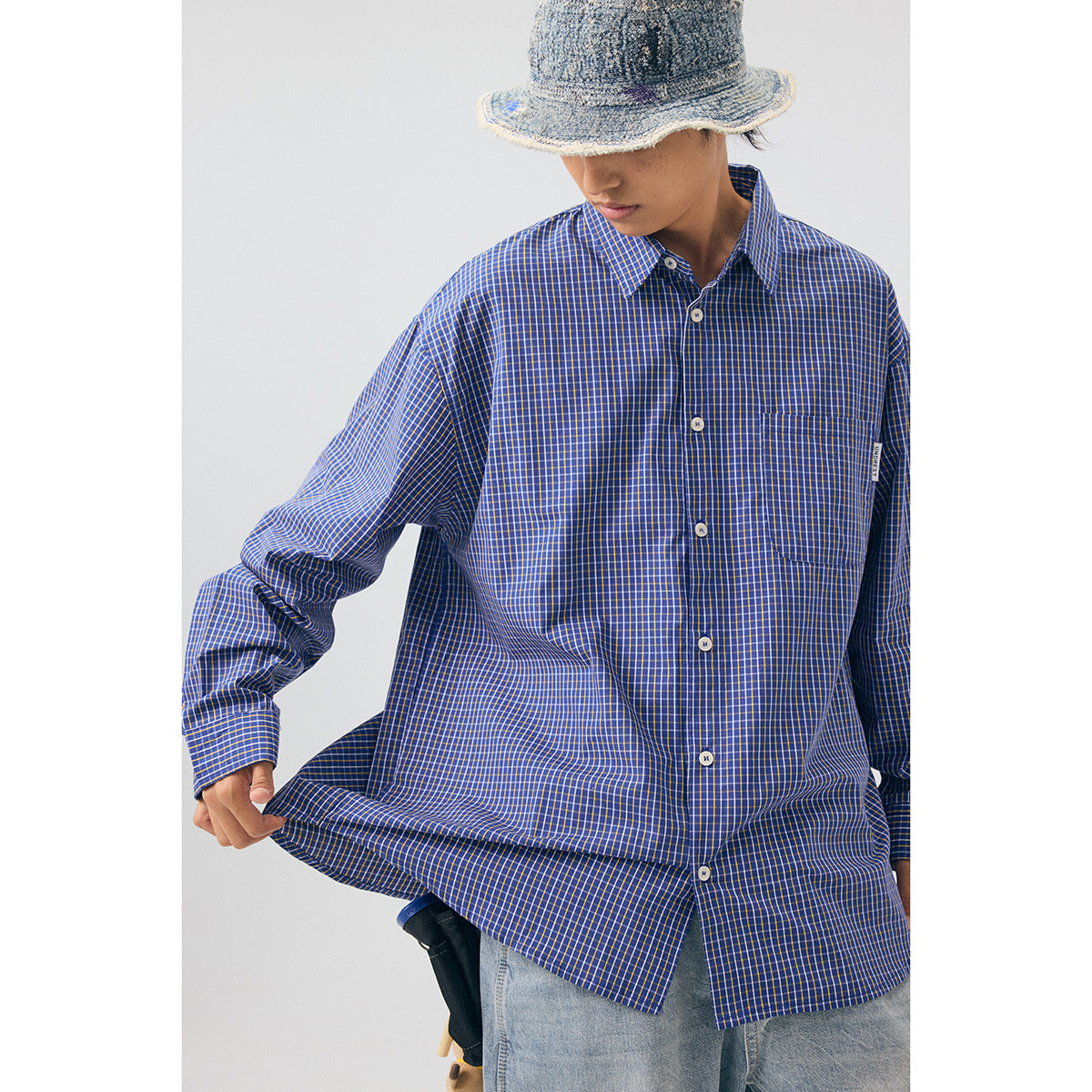 Model wearing an oversized blue checked button-up shirt with a chest pocket and white buttons.