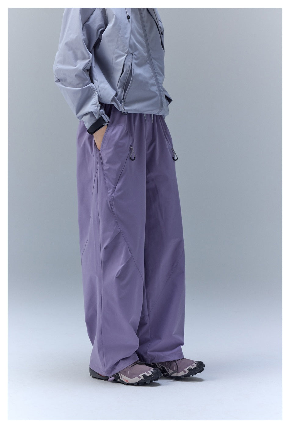 Side view of a person wearing loose lavender-purple pants with curved seam panels and zip pockets.