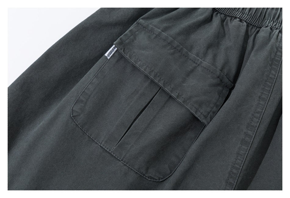 Close-up of a large patch pocket on dark charcoal pants, with a small sewn label at the edge.