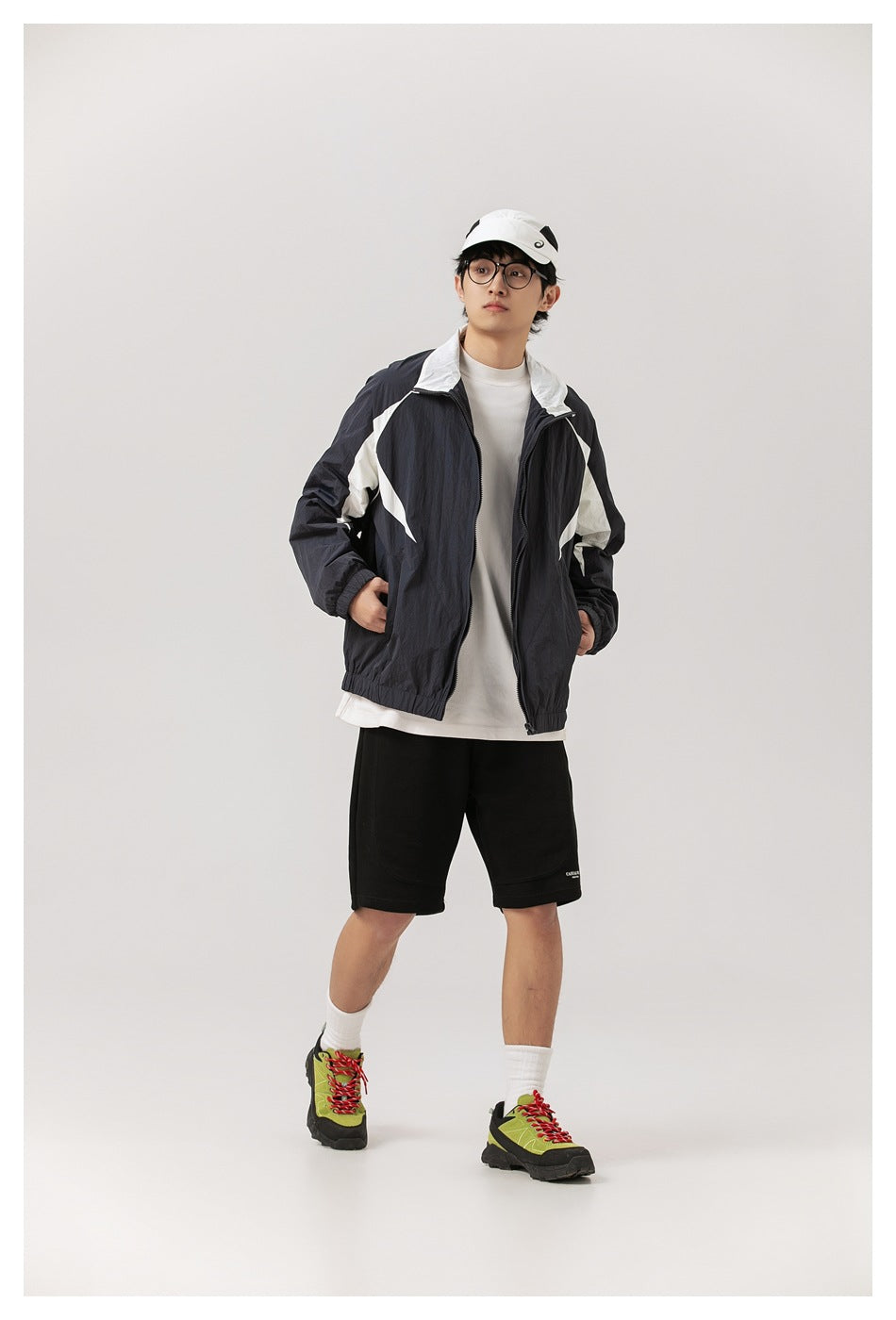 Full-length view of a model wearing the navy and white color-block jacket open with black shorts and green sneakers