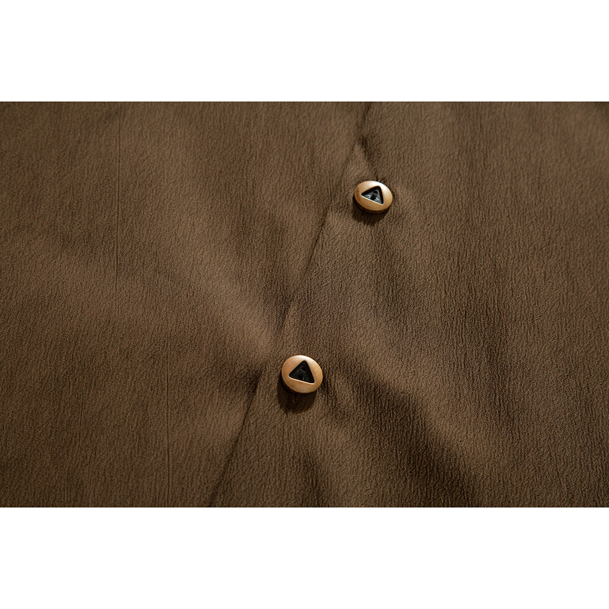 Close-up of two tan buttons with dark triangular centers on a brown shirt.