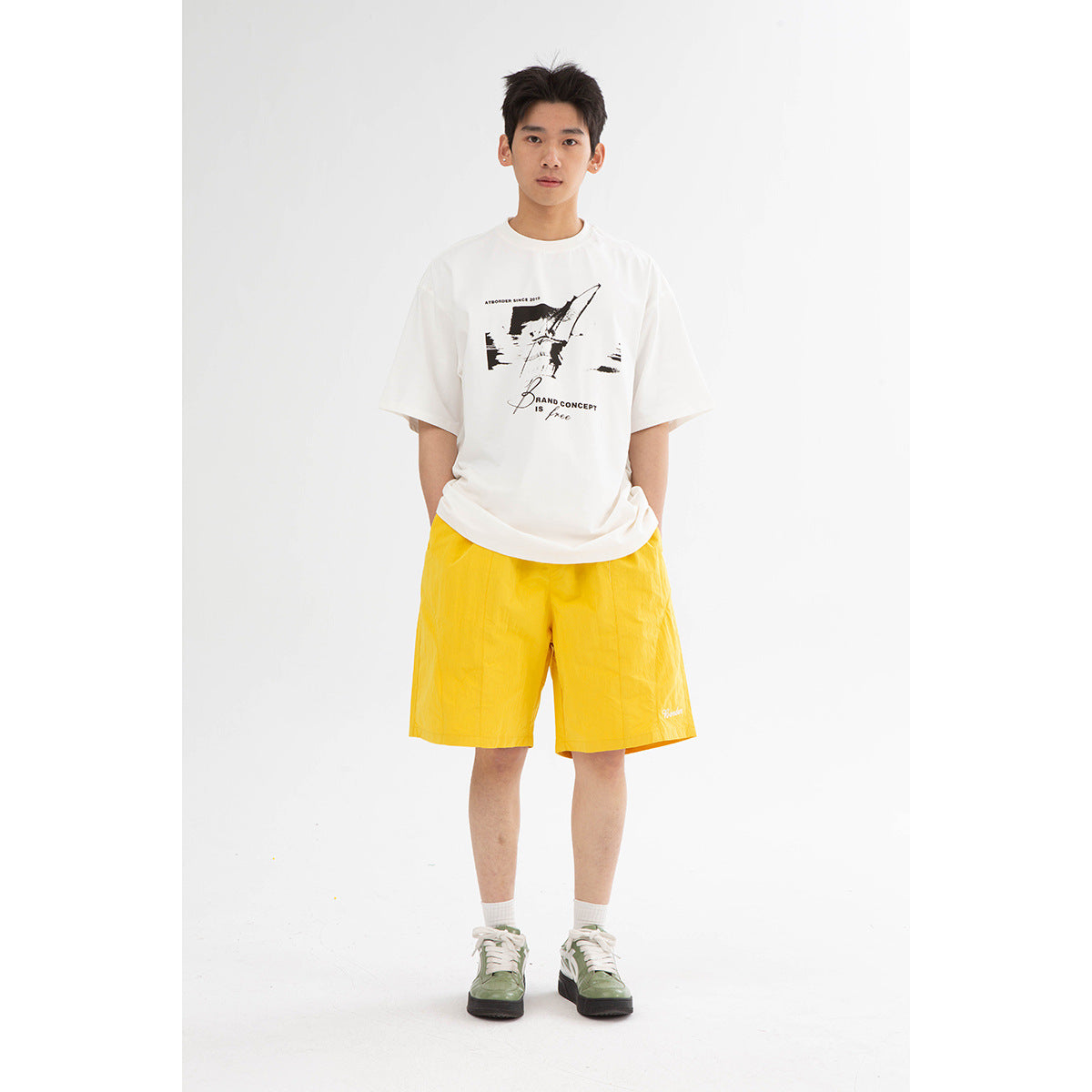 A model wears a white graphic T-shirt and bright yellow knee-length shorts.