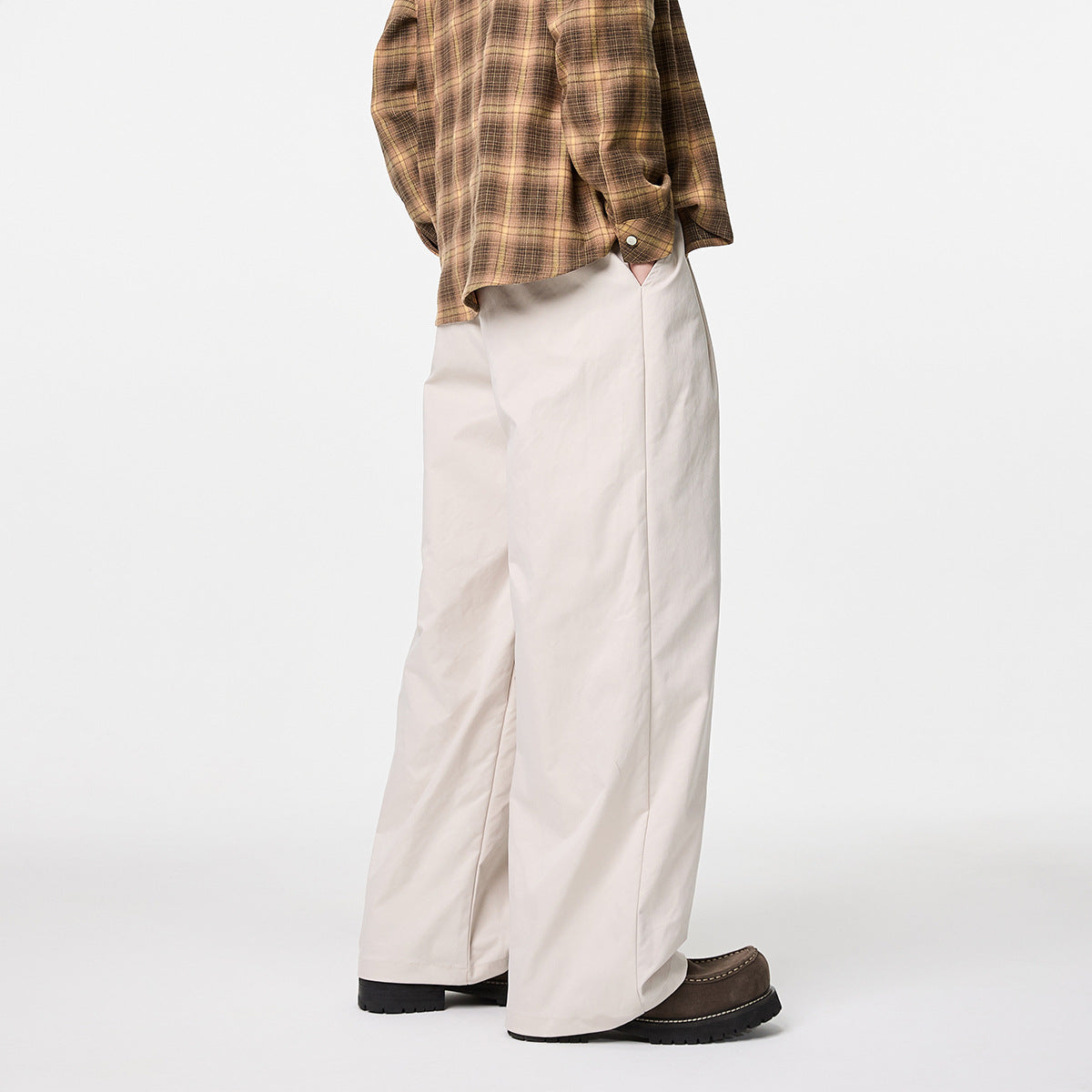 Side view of a model wearing ivory wide-leg trousers with a brown plaid shirt and dark shoes.