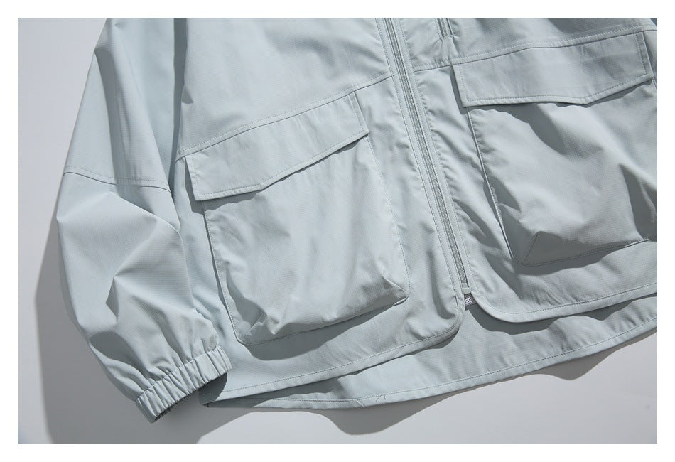 Close-up of the pale gray jacket's front, showing two large flap pockets, a central zipper, and an elastic cuff.