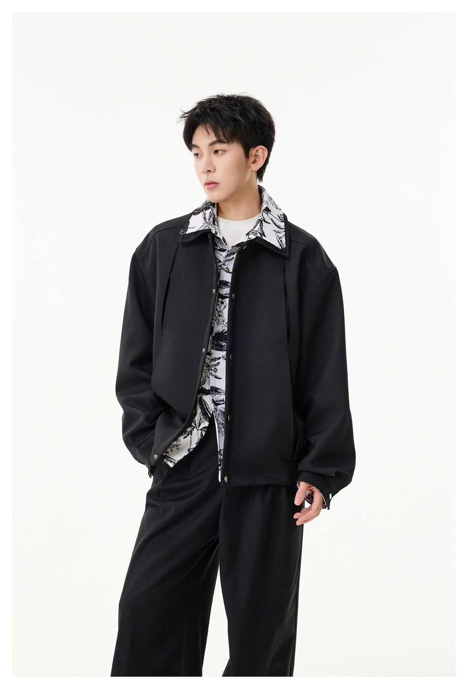 Man modeling a black jacket with silver snaps and contrasting black-and-white botanical print at the collar and placket.