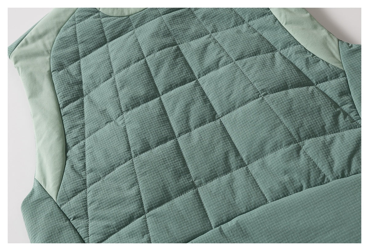 Close-up of a sage green garment with dark square quilting and lighter green curved panels.