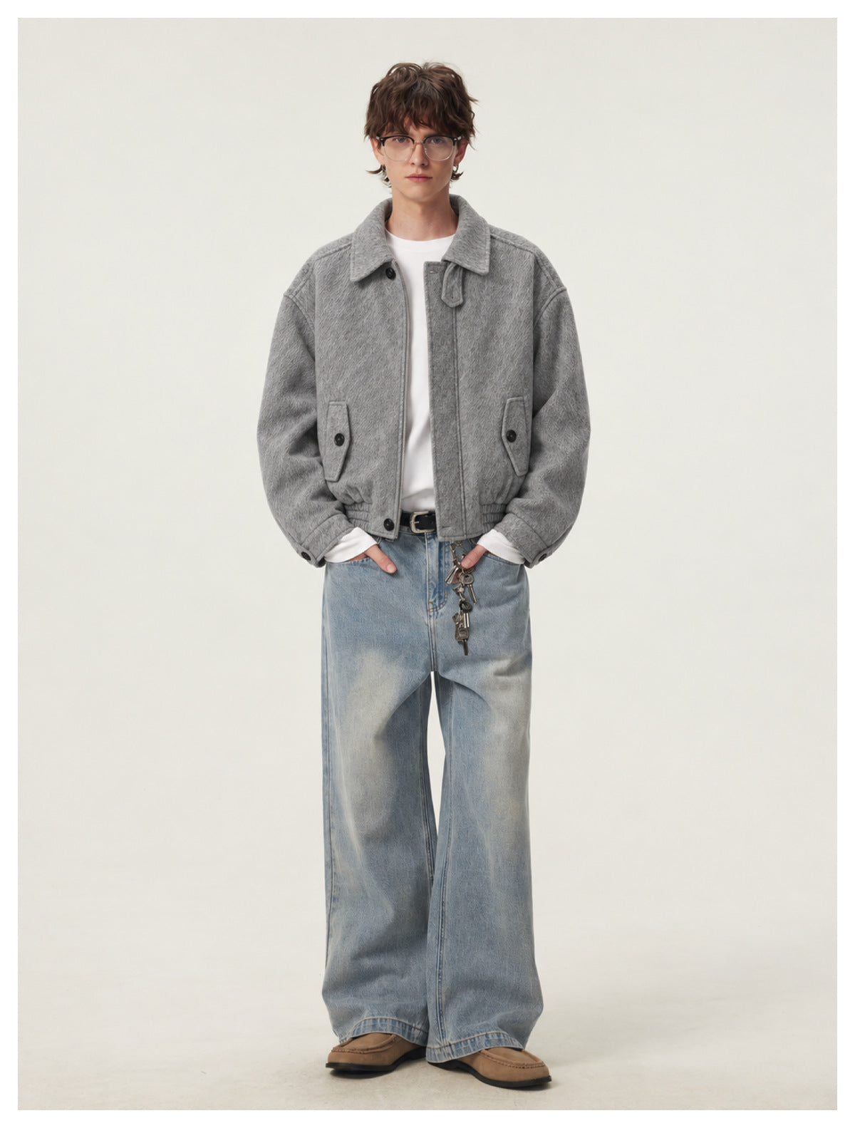 Full-length front view of a model wearing a gray textured jacket, white shirt, loose blue jeans, and brown shoes.