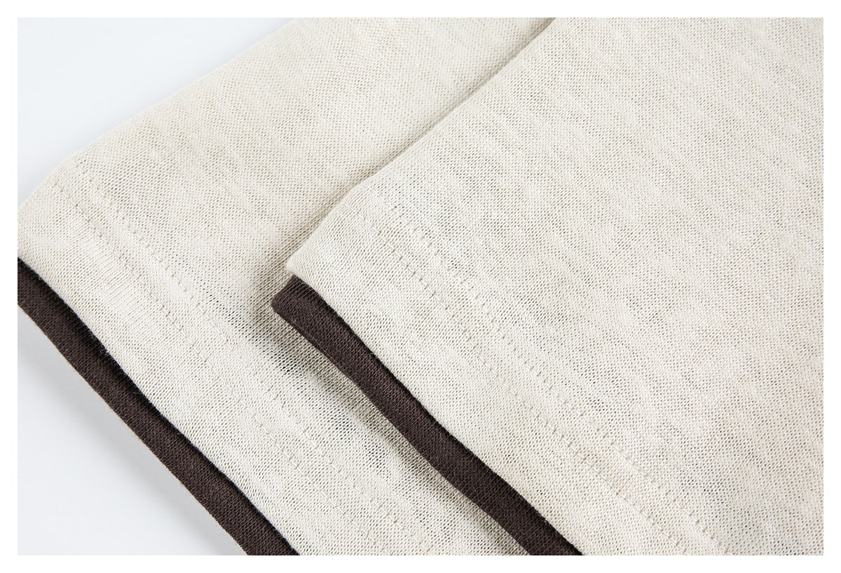 Close-up of cream knit fabric folded to show dark brown edging and parallel stitching.