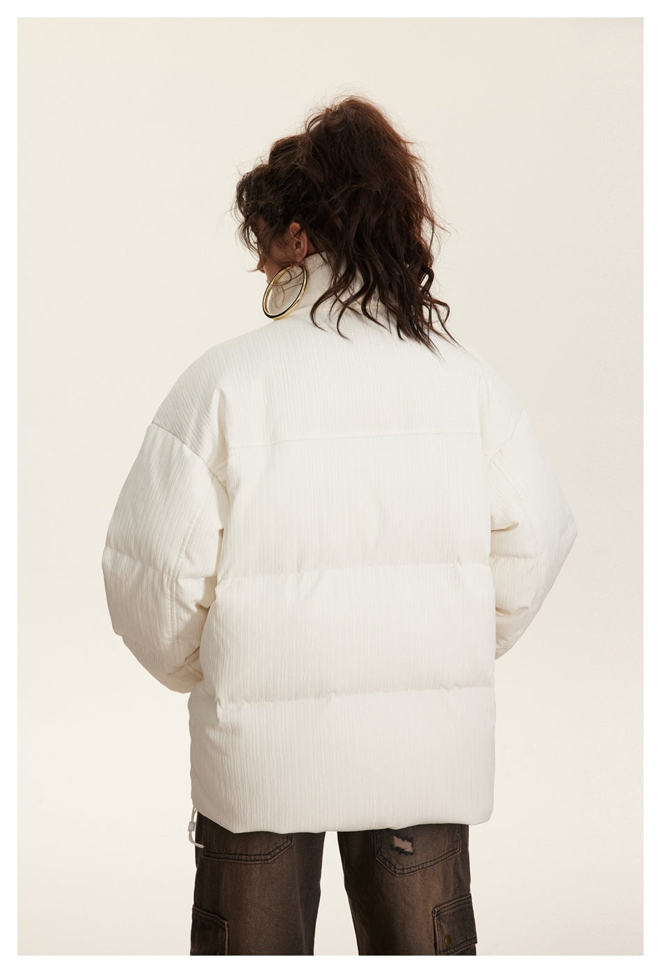 Back view of a model wearing an ivory quilted puffer jacket with a high collar and horizontal padded panels.