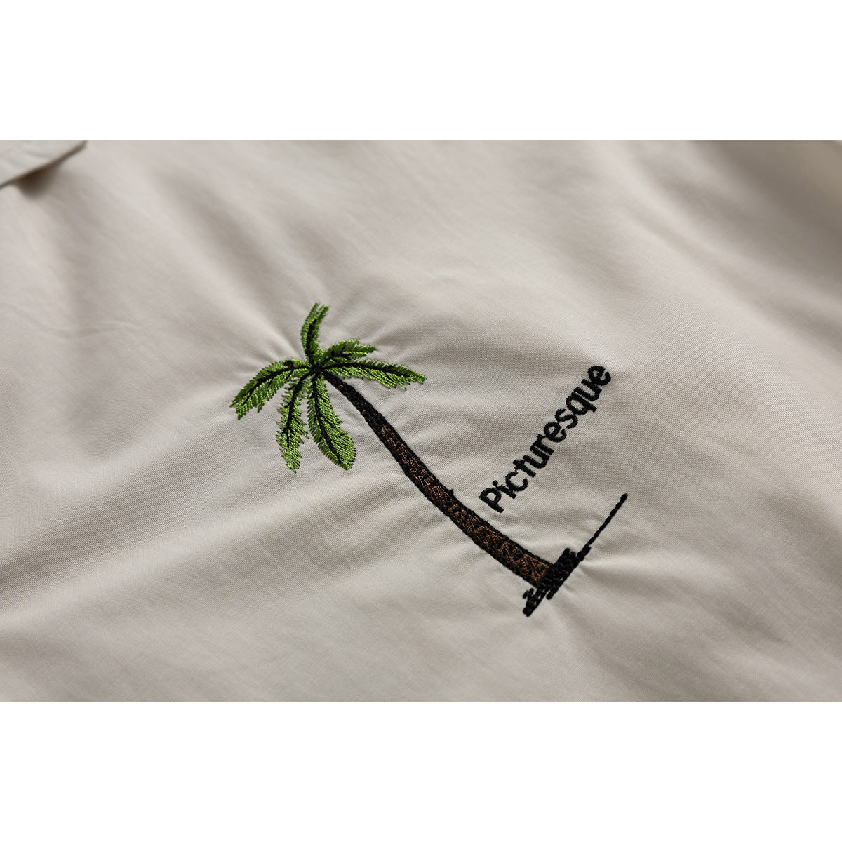 Close-up of a palm tree and the word “Picturesque” embroidered on ivory fabric.
