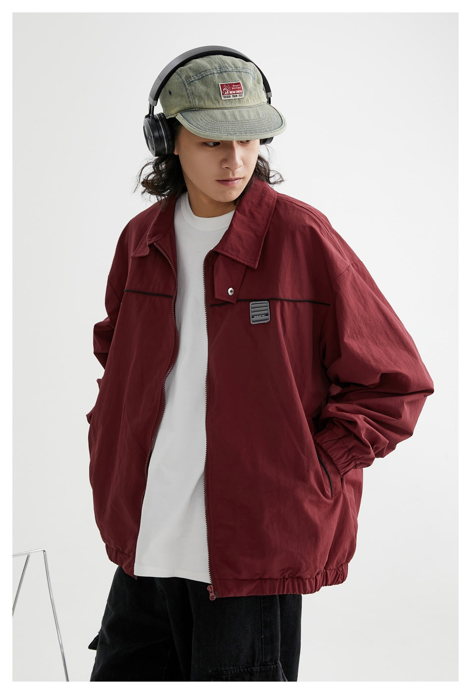 Close view of a model wearing a burgundy zip jacket with black chest trim and a sage cap with headphones.