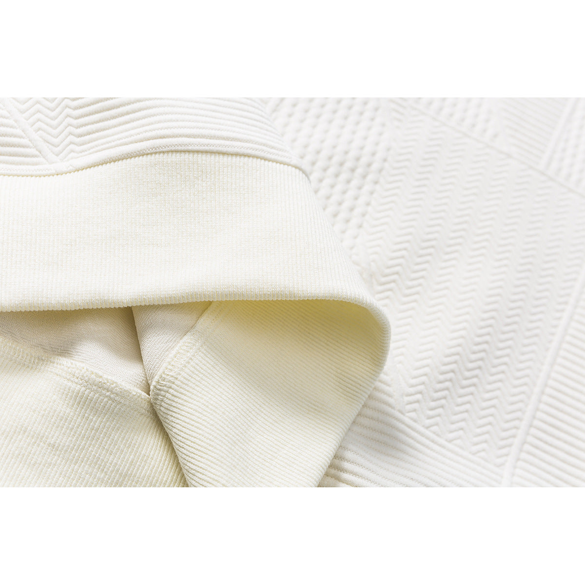 Close-up of an ivory pullover's ribbed sleeve cuff beside its raised geometric pattern.