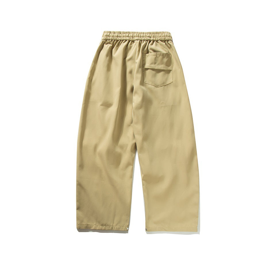 Back view of loose tan trousers with an elastic waist and a patch pocket.