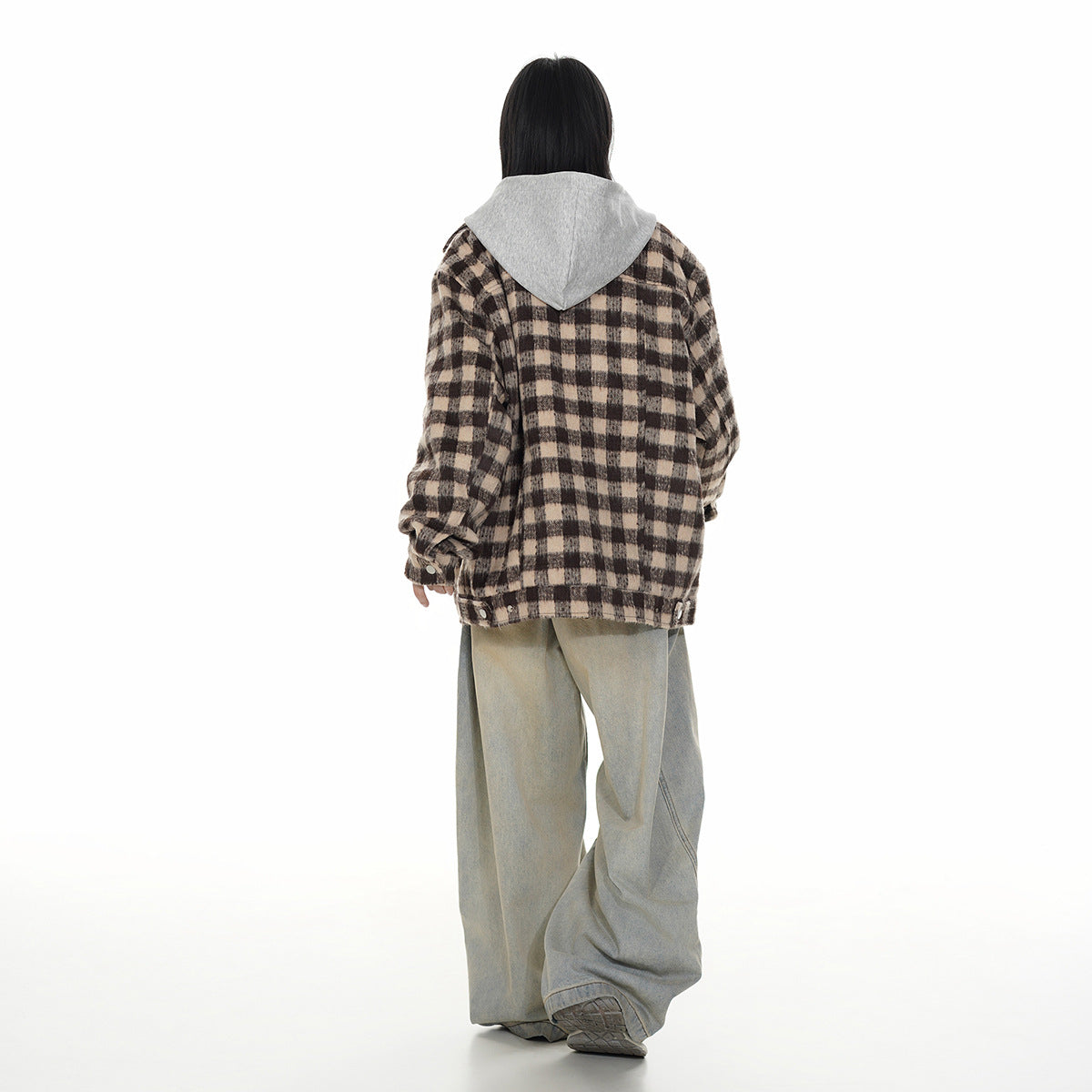 Back view of a model wearing a brown and black plaid hooded jacket with loose light-wash jeans.