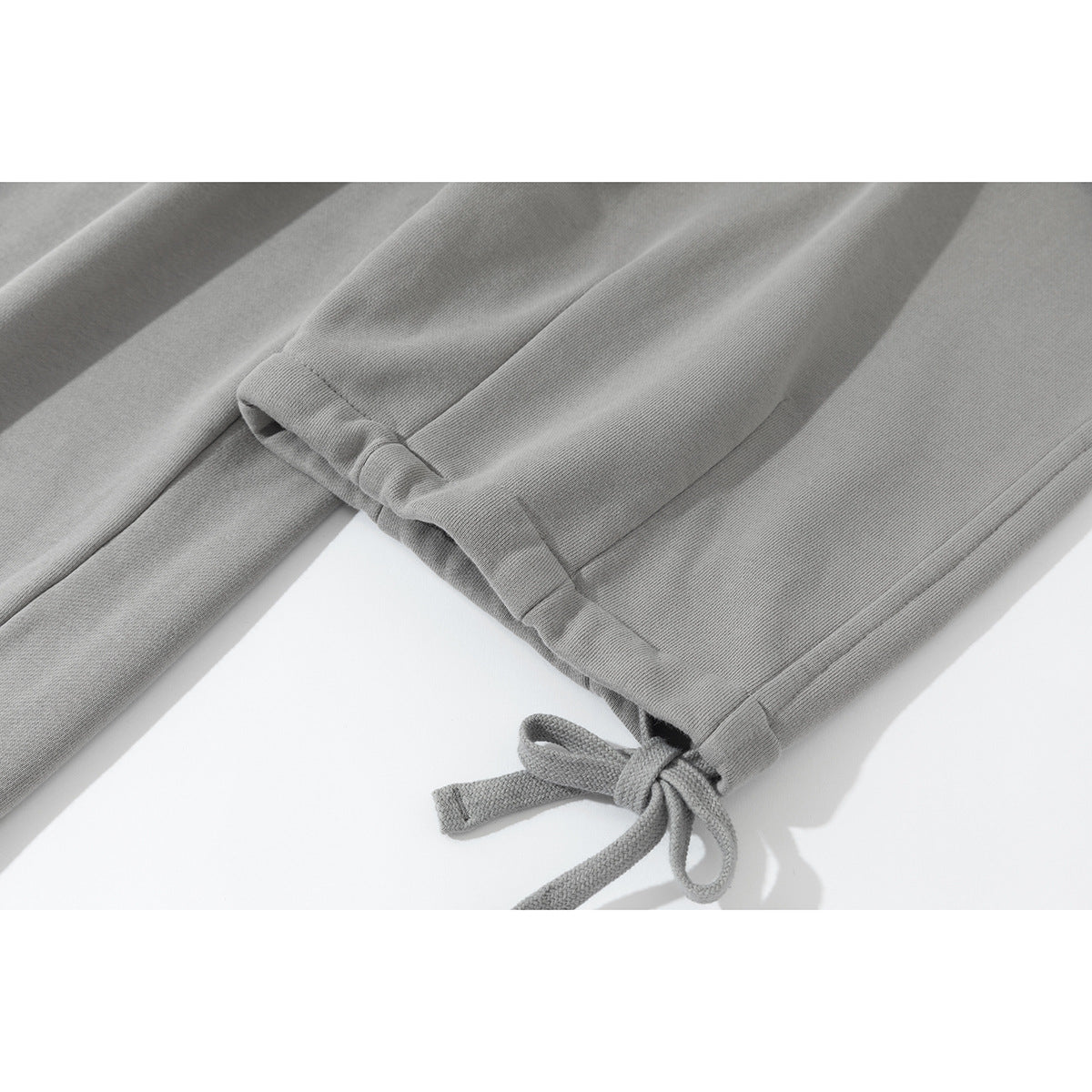 Close-up of light gray pant legs with adjustable tie details at the cuffs.