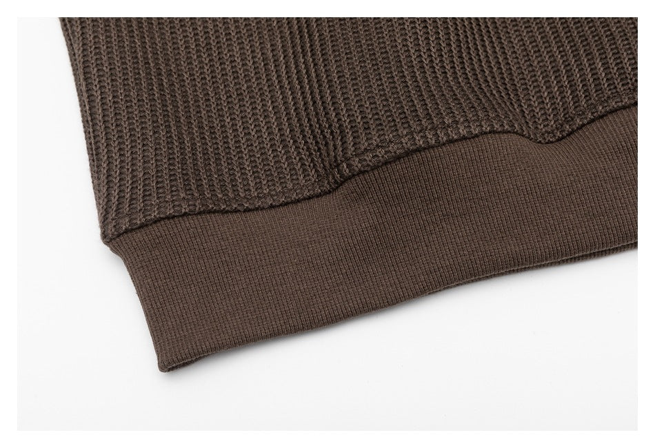 Close-up of the dark brown sweater's chunky knit sleeve and ribbed cuff.
