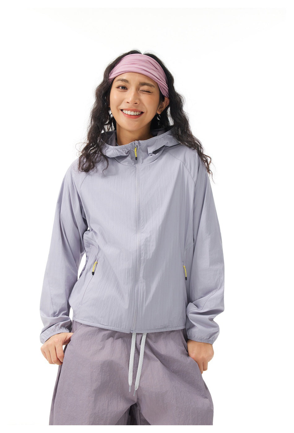 Front view of a model wearing a light gray-lavender hooded jacket with zip pockets and loose matching trousers.