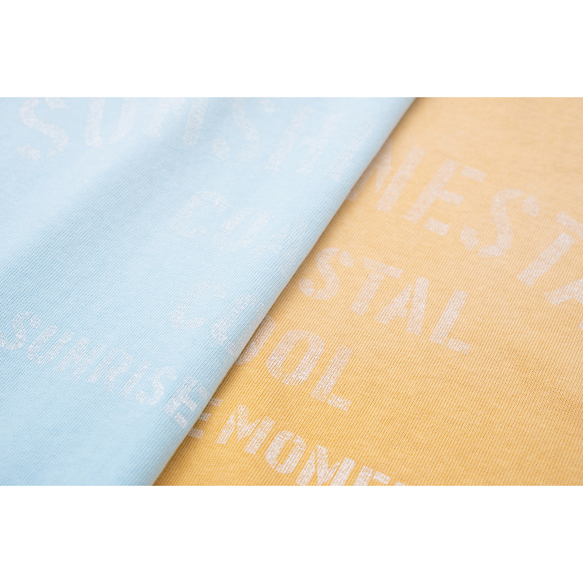 Close-up of light blue and golden-yellow T-shirt fabric with faint printed lettering.