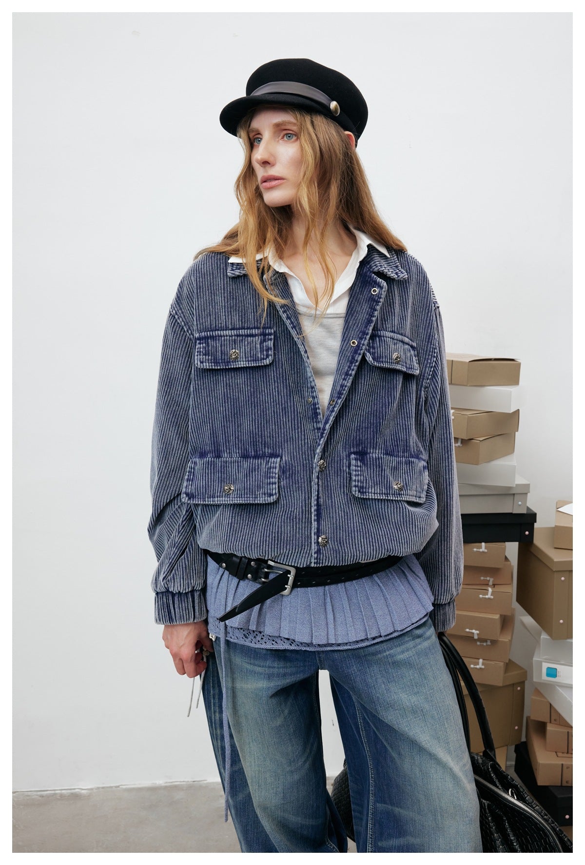 Model wearing a blue-gray ribbed jacket with four button-flap pockets, styled over a layered top and wide-leg jeans.