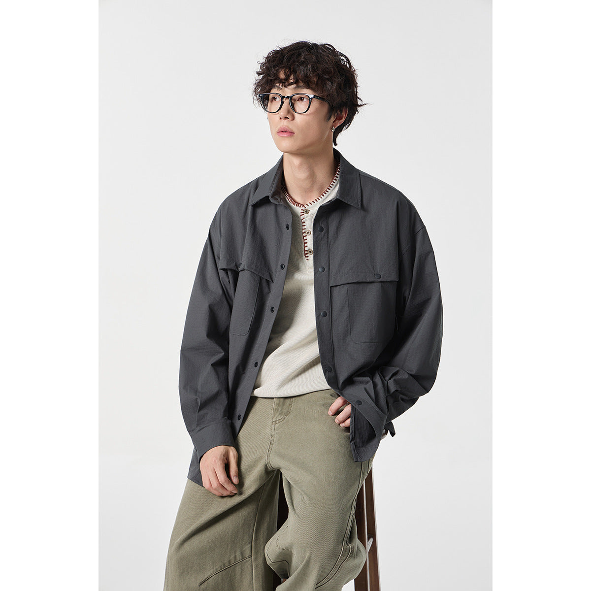 Model wearing a charcoal oversized button-up shirt with flap chest pockets and olive pants.