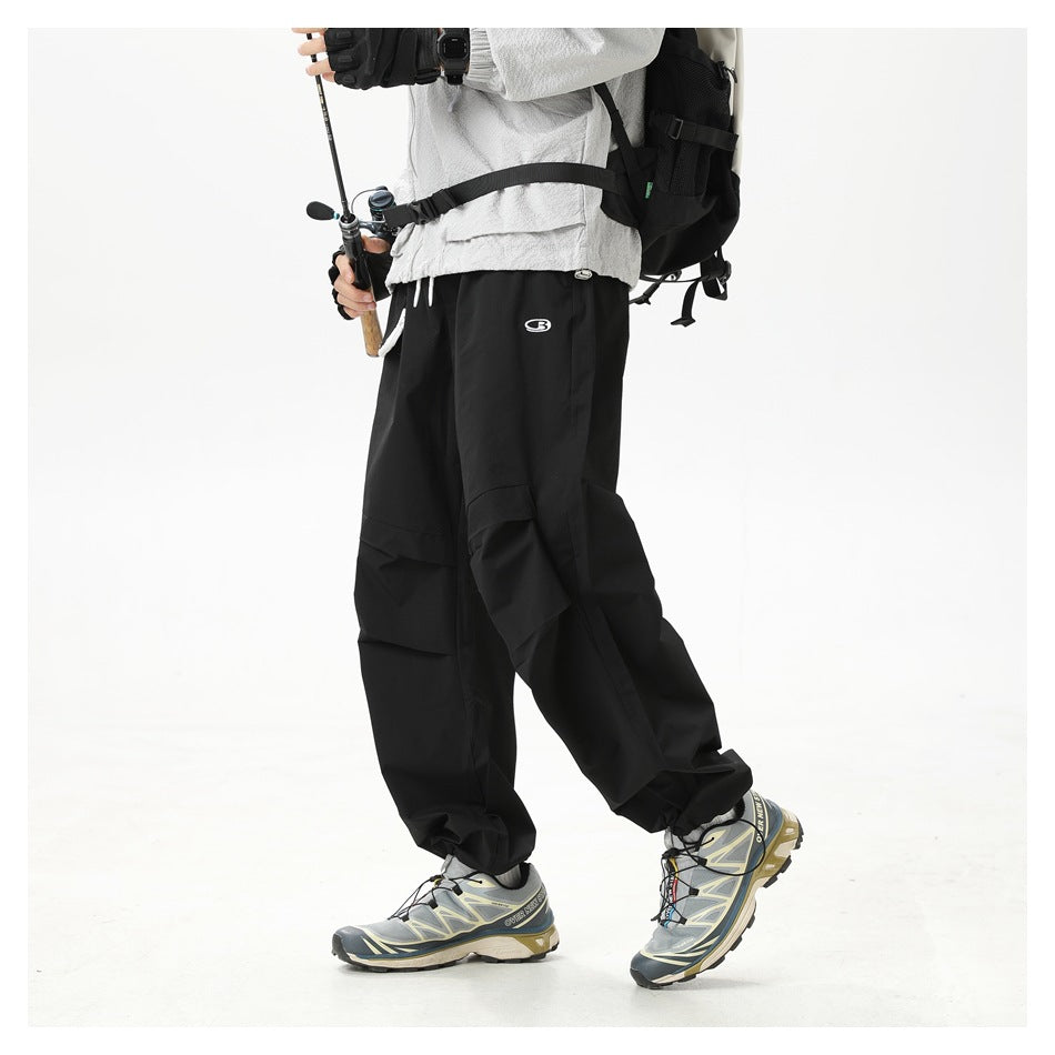 Side view of a cropped model wearing black loose cargo pants with layered pockets and hiking shoes.